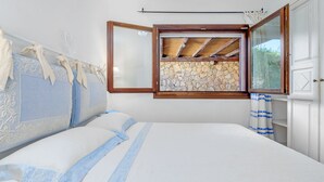 A bedroom with a bed, a window with a stone wall view, and a white door. - Casa Maestrale 6, Emma Villas (Palau)