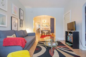 Una sala de estar con sofá, mesa de centro, estantería y televisor.