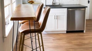 A kitchen with a wooden table and chairs, a dishwasher, and pendant lights.