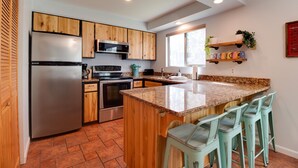 A modern kitchen with wooden cabinets, stainless steel appliances, a granite countertop, and bar stools.