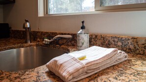 A kitchen with a granite countertop, a stainless steel sink, a bottle of hand soap, and a folded towel.