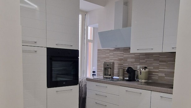 A modern kitchen with white cabinetry, a built-in oven, and a coffee machine.