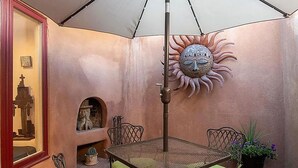 Een terras met een metalen tafel en stoelen, een decoratieve zon en een kleine open haard.