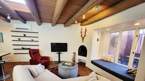 Een woonkamer met een rode fauteuil, een witte bank, een televisie, een open haard en een groot raam.