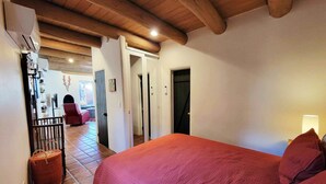 Een slaapkamer met een houten plafond, een rode sprei en uitzicht op een eetgedeelte met een rode stoel.