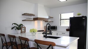 A modern kitchen with a central island, bar stools, a microwave, and a black refrigerator.