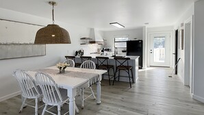A modern kitchen with white cabinetry, a central island, and a dining area with white chairs and a table.