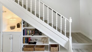 A staircase with white balusters and a wooden handrail, leading to a landing with a shelf holding books and decorative items.