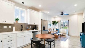 A modern kitchen with white cabinets, a dining area with two chairs, and a ceiling fan.