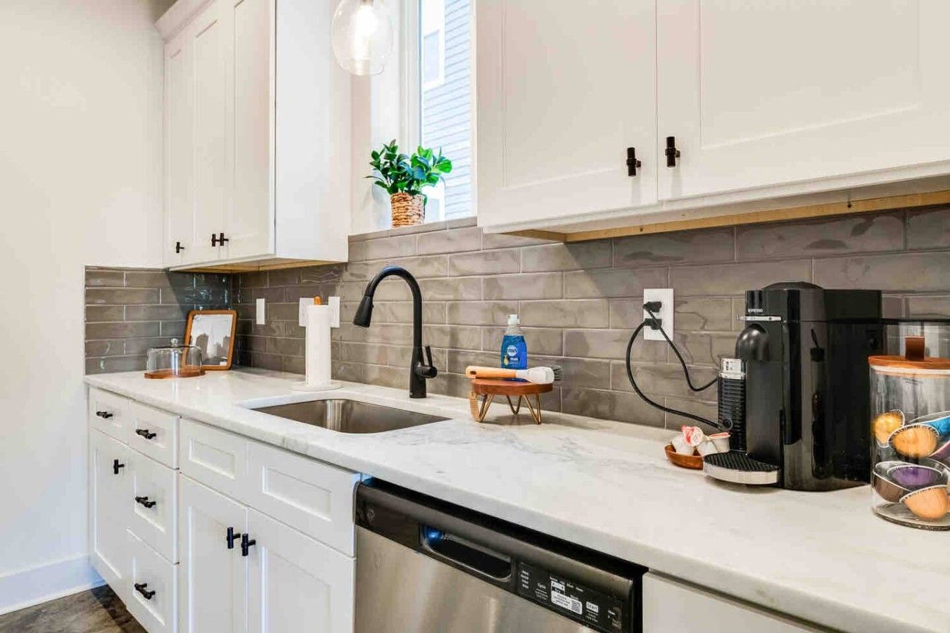 A modern kitchen with white cabinets, a stainless steel dishwasher, a coffee machine, and a sink with a black faucet.