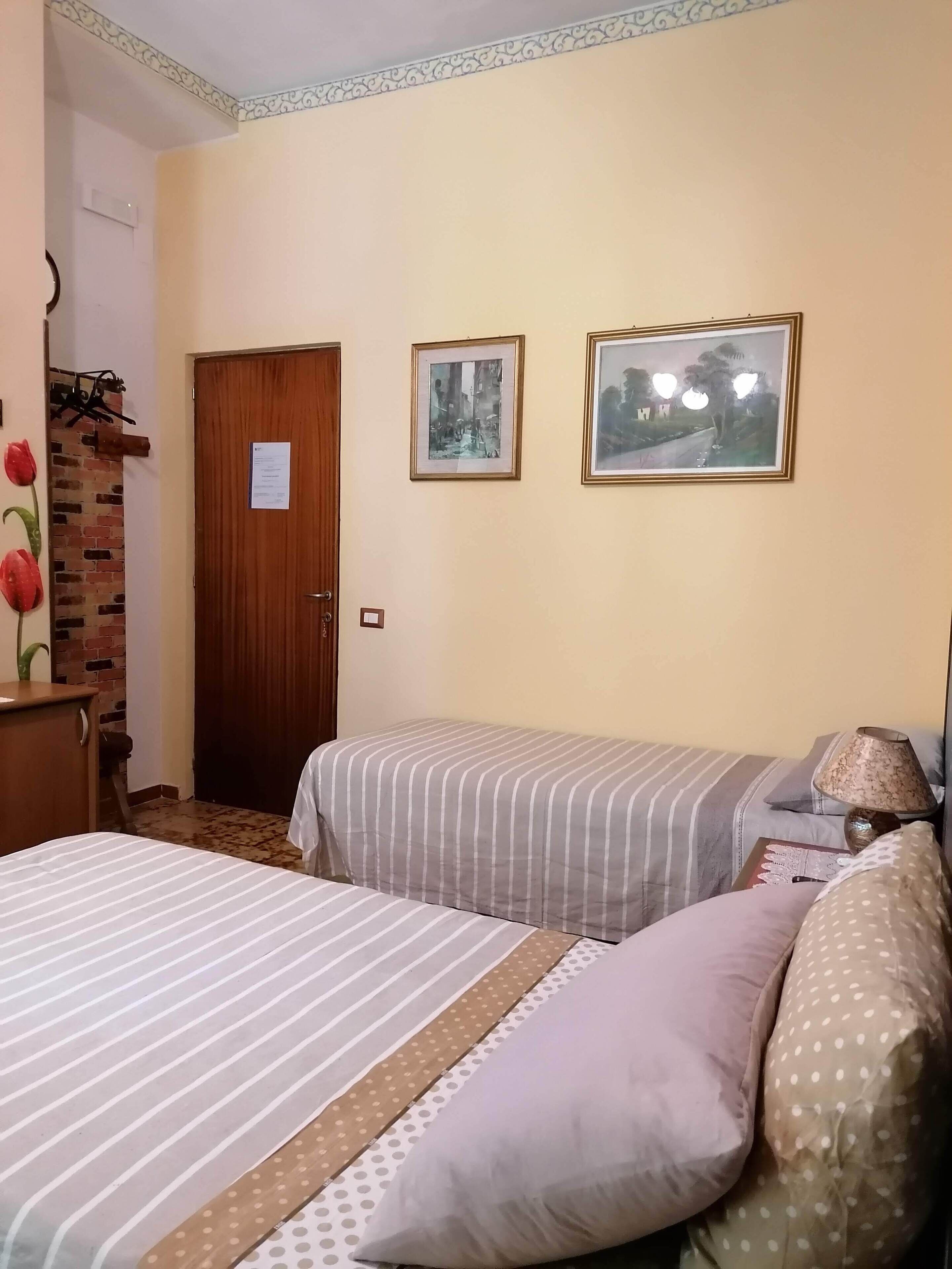 A hotel room with two beds, a wooden door, and two framed pictures on the wall.