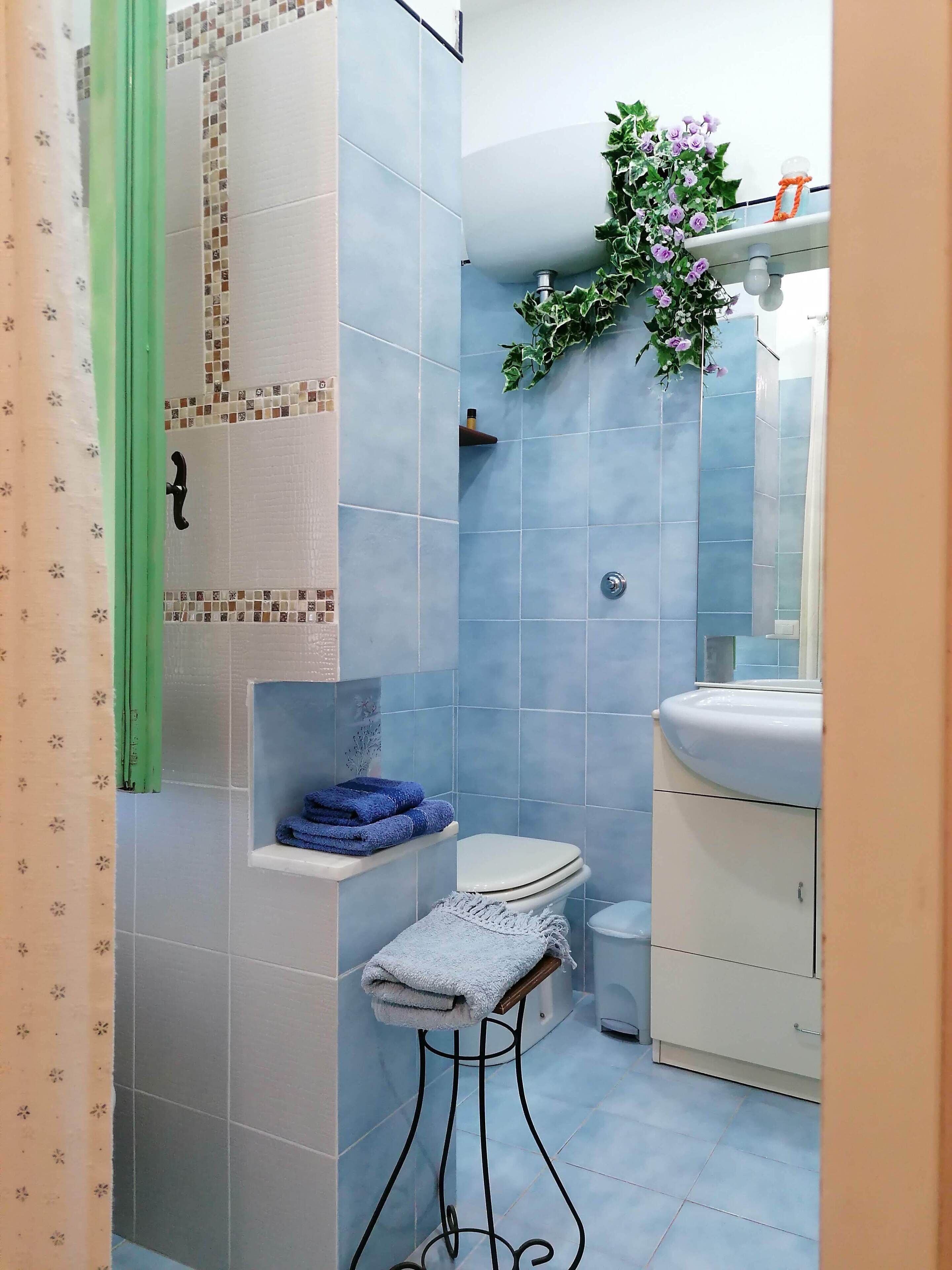 Un baño con inodoro, lavamanos y un estante con toallas dobladas.
