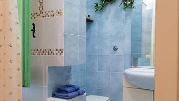Un baño con inodoro, lavamanos y un estante con toallas dobladas.