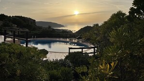 Ein Pool mit Blick auf den Sonnenuntergang über dem Meer, umgeben von Grünflächen und Hügeln.