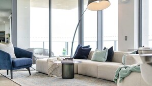 Una sala de estar moderna con sofá, sillón, mesa de centro, ventanas amplias y una lámpara de pie.