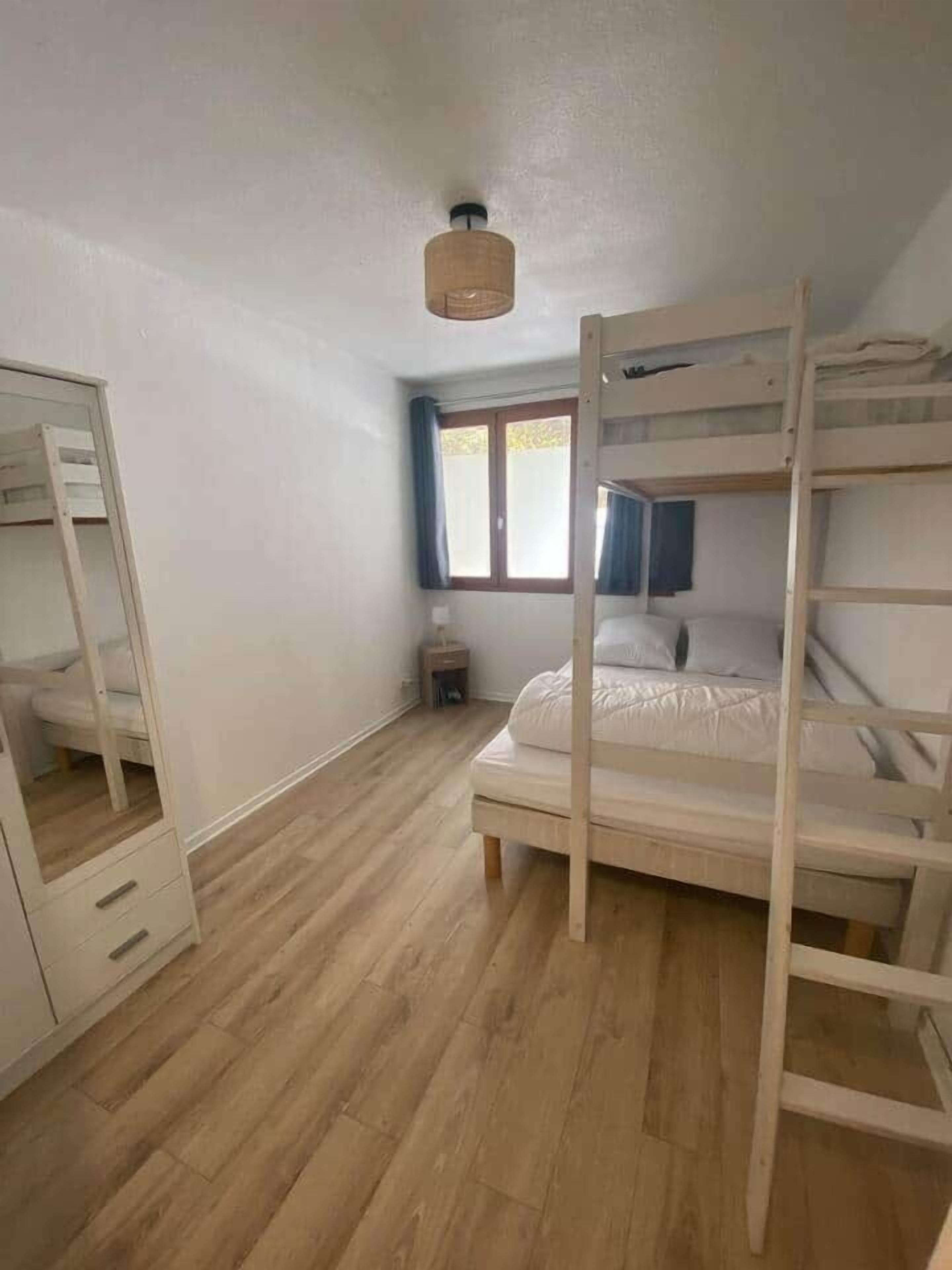 A room with a bunk bed, a wooden wardrobe, a small bedside table, and a window with curtains.