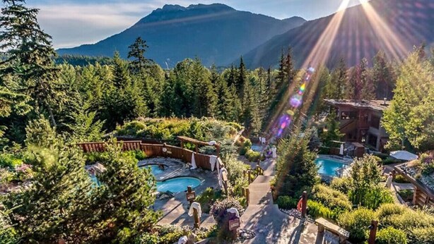 Un resort con varias piscinas, rodeado de un bosque denso y montañas.
