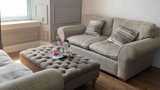 A living room with a sofa and ottoman, a window, and a lamp. - The Victorian Apartment (Dundee)