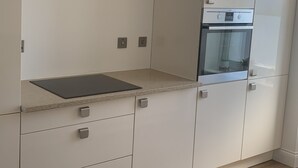 A modern kitchen with white cabinetry, a built-in oven, and a granite countertop. - The Victorian Apartment (Dundee)