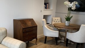 A dining area with a wooden table, white upholstered chairs, a wooden cabinet, and a television mounted on the wall. - The Victorian Apartment (Dundee)
