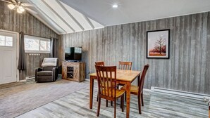 Ein Essbereich mit einem Holztisch und Stühlen, einem Fernseher auf einer Holzkommode und einem gerahmten Bild an der Wand.