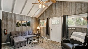 Ein gemütliches Wohnzimmer mit einer Eckcouch, einem kleinen Couchtisch, einem Kamin und einem großen Fenster mit Vorhängen.