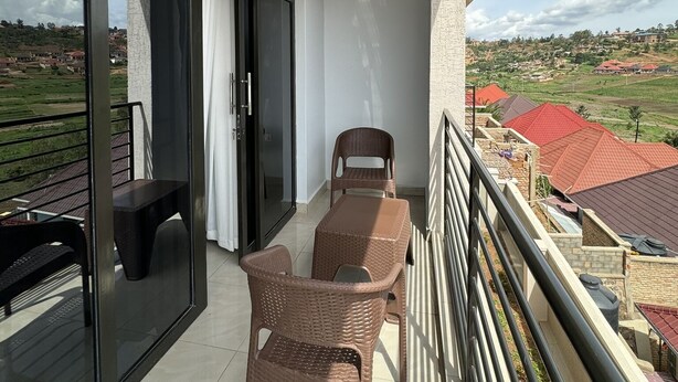 Een balkon met rieten meubilair, een tafel en uitzicht op huizen en groen.