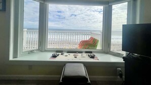 A room with a bay window overlooking a beach. There is a small bench with decorative items in front of the window. - Oceanfront Wells Beach Condo - Ocean Surf #6 (Wells)