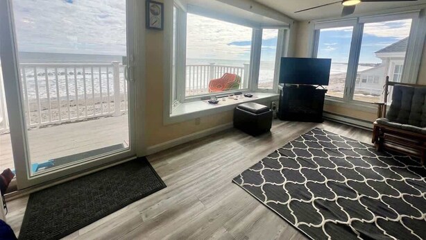 A room with large windows, a ceiling fan, a TV, and a view of the beach. - Oceanfront Wells Beach Condo - Ocean Surf #6 (Wells)