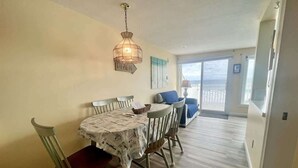 A dining area with a table and chairs, a hanging light fixture, and a view of the ocean through large windows. - Oceanfront Wells Beach Condo - Ocean Surf #6 (Wells)