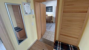 A hallway with a wooden floor, a door with a mirror, a telephone, and a wall-mounted notice board.