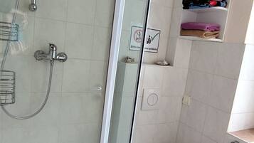A modern bathroom with a glass-enclosed shower, a toilet, and a shelf with folded towels.