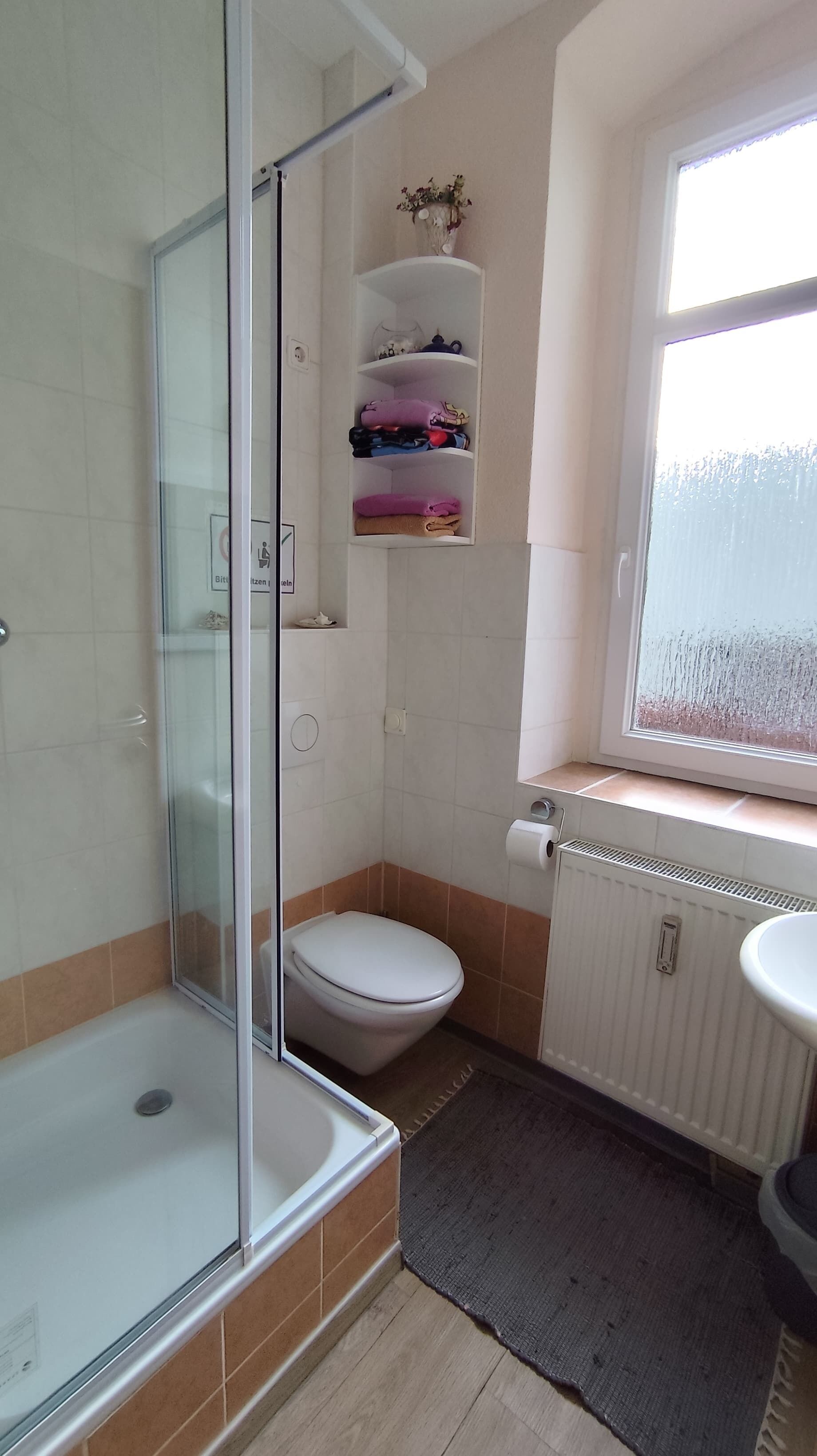 A bathroom with a glass shower enclosure, a toilet, a radiator, and a window with a view.