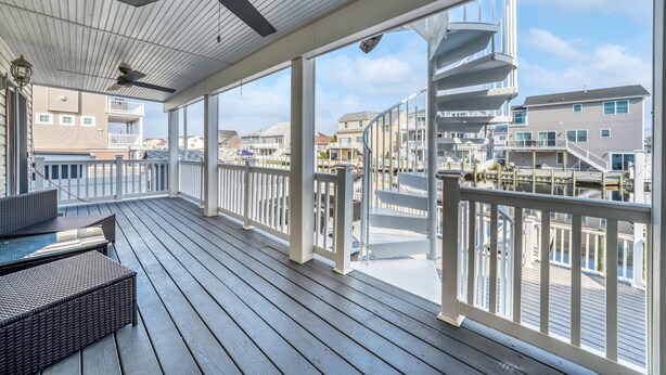 A covered outdoor deck with a view of the waterfront, featuring a railing, seating area, and a ceiling fan. - Waterfront w/dock & hot tub, bring your boat/jet ski-5 minutes from beach-LBI!!! (Manahawkin)