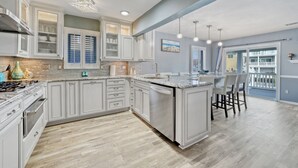 A modern kitchen with white cabinetry, a central island, and a dining area with chairs. - Waterfront w/dock & hot tub, bring your boat/jet ski-5 minutes from beach-LBI!!! (Manahawkin)