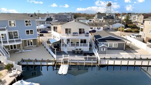A waterfront property with a dock, a covered outdoor seating area, and a multi-level house with a balcony. - Waterfront w/dock & hot tub, bring your boat/jet ski-5 minutes from beach-LBI!!! (Manahawkin)