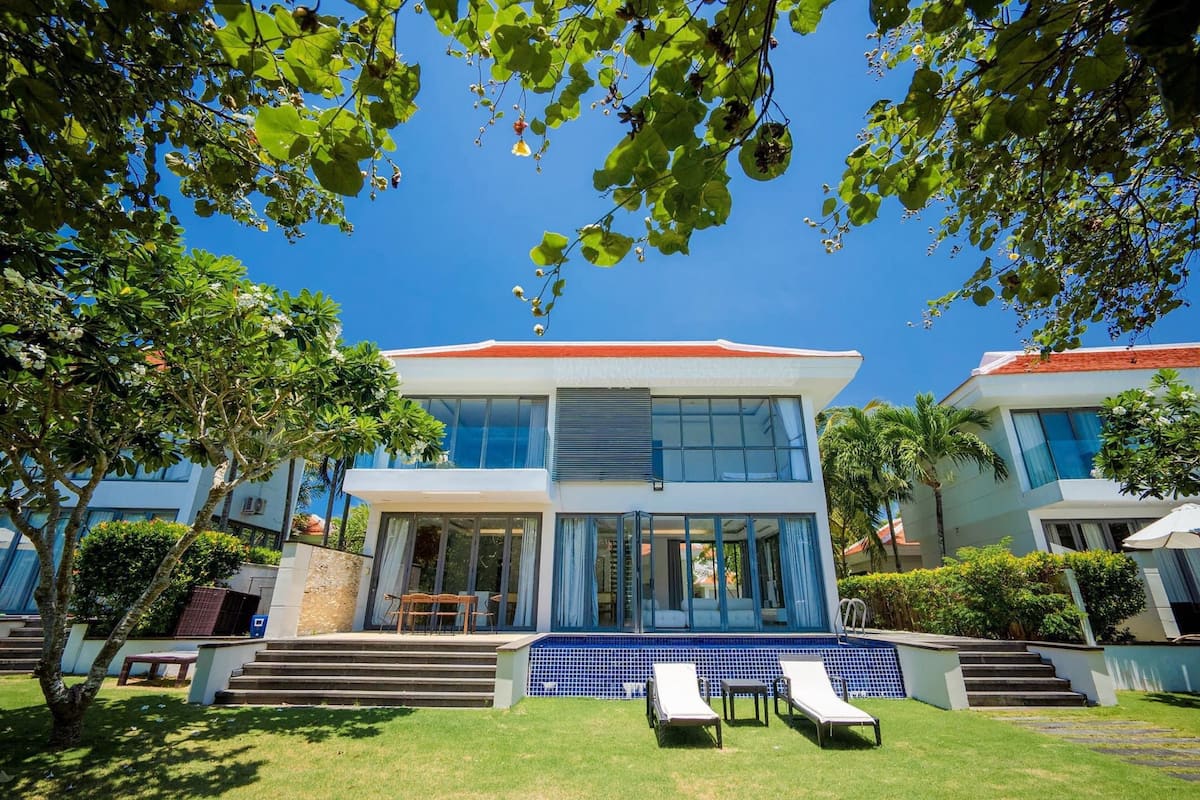 A modern two-story building with large windows, a swimming pool, and a well-maintained lawn.