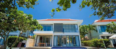 A modern two-story building with large windows, a swimming pool, and a well-maintained lawn.
