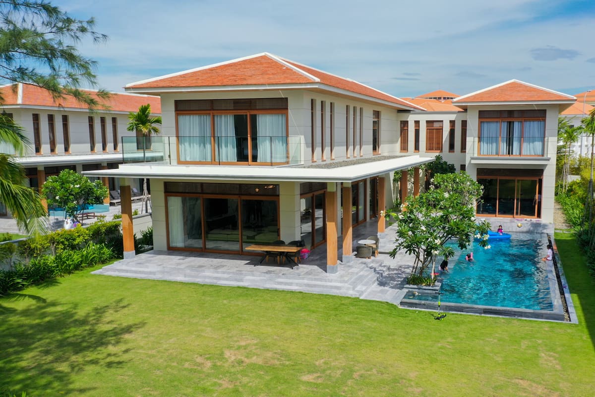 A modern two-story house with a swimming pool, surrounded by lush greenery and palm trees.