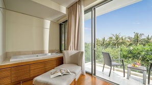 A modern bathroom with a large bathtub, a wooden vanity, and a bench with a magazine. - The Ocean Suites (Da Nang)