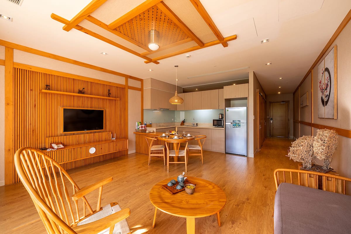 A modern living room with wooden furniture, a flat-screen TV, and a dining area with a kitchen in the background.