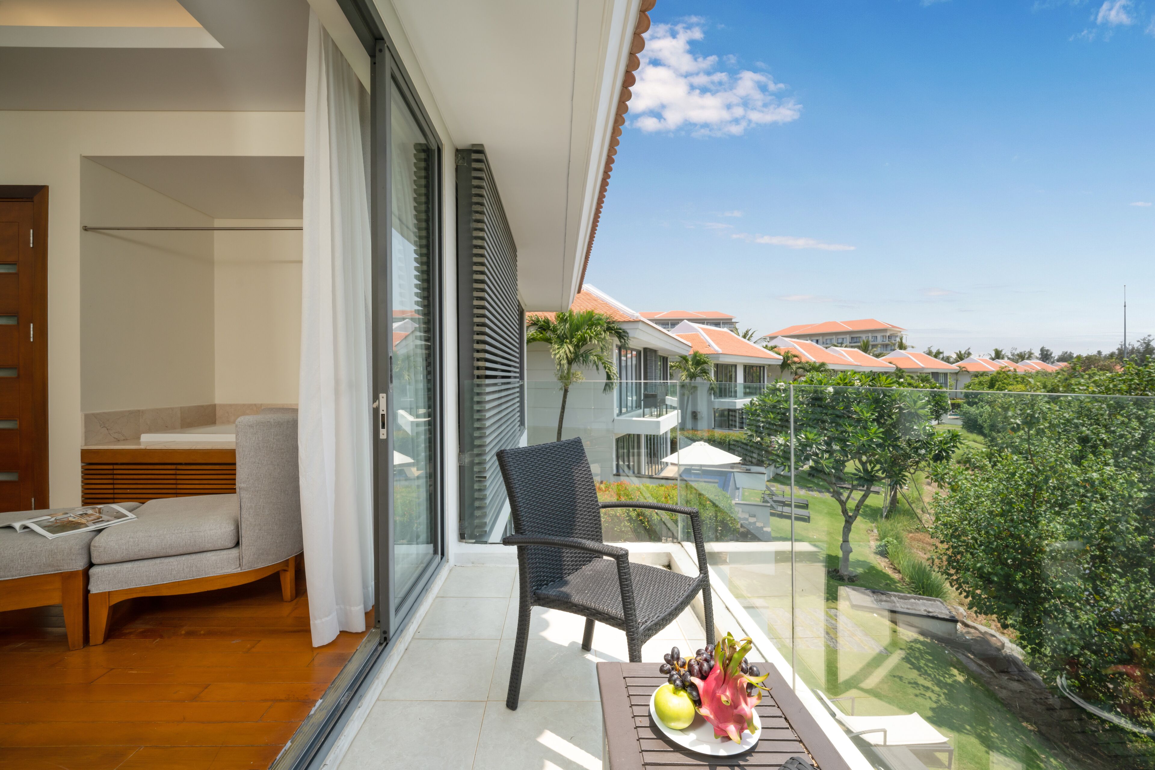 A balcony with a chair, a table with fruit, and a view of houses and greenery.