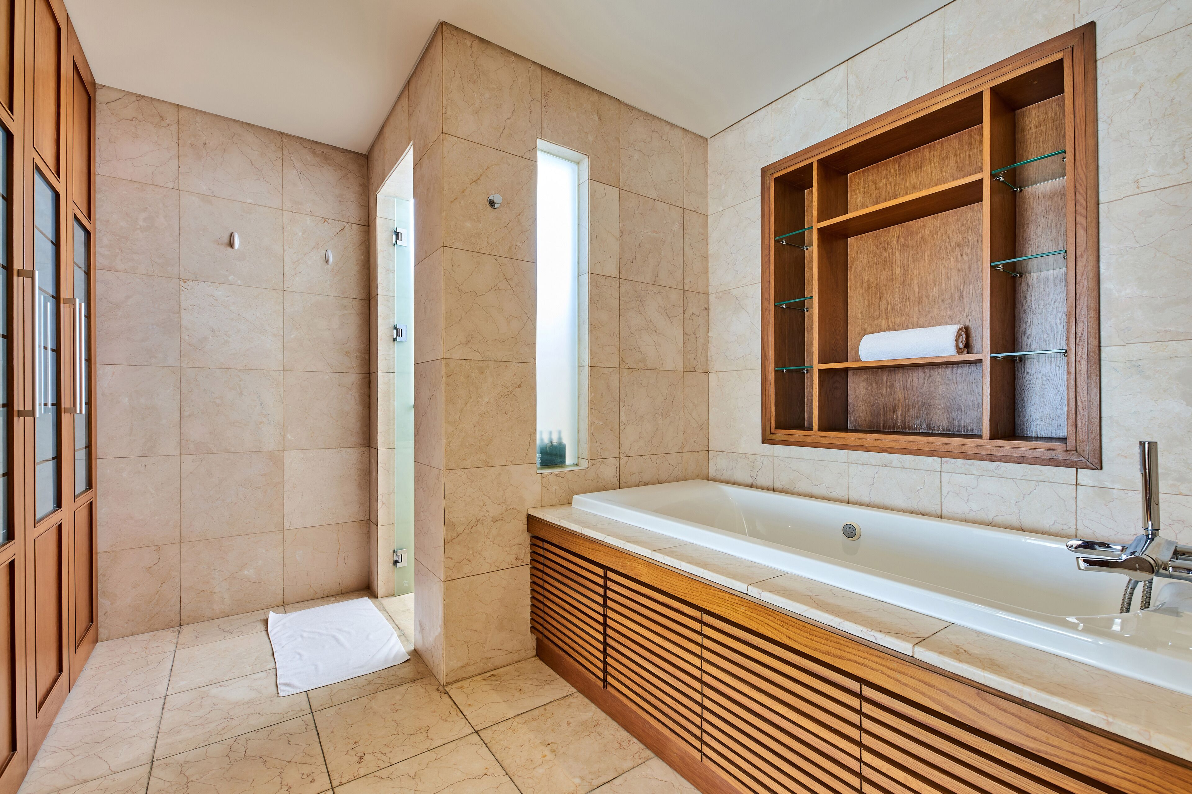 A modern bathroom with a large bathtub, wooden vanity, and a built-in shelf with a towel.