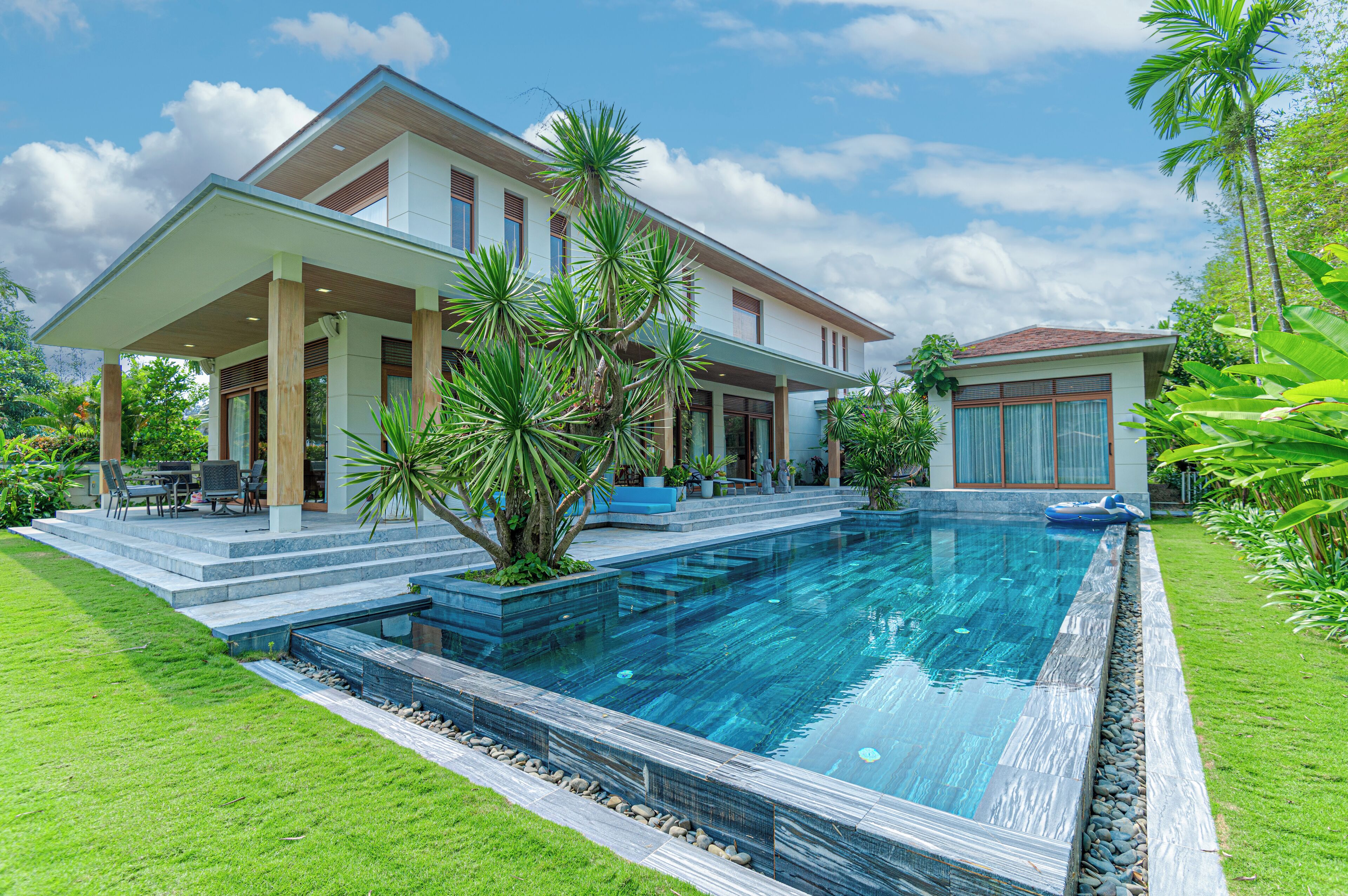 A modern house with a swimming pool, a covered patio, and lush greenery.