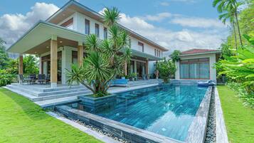 Una casa moderna con piscina, un patio cubierto y abundante vegetación.