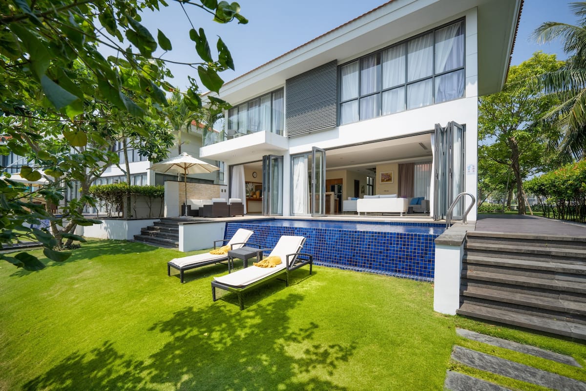 A modern two-story house with a swimming pool, outdoor seating, and a well-maintained lawn.