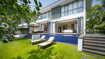Una casa moderna de dos pisos con piscina, mobiliario exterior y un césped cuidado.