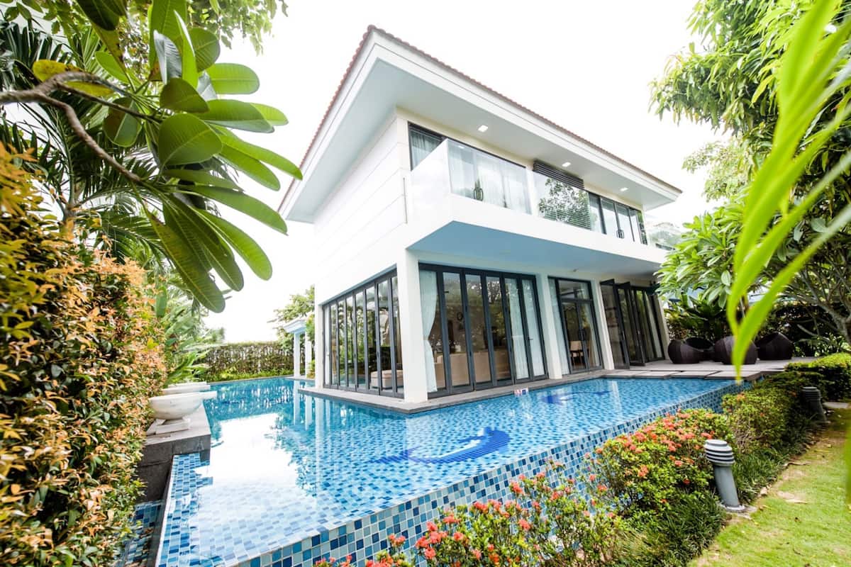 A modern two-story house with a large glass balcony overlooking a swimming pool.