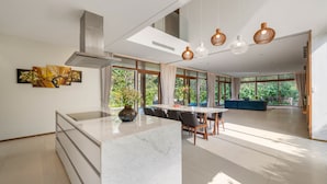 A modern kitchen with a marble island, large windows, and a dining area with a blue sofa. - The Ocean Suites (Da Nang)