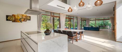 Una cocina moderna con una isla de mármol, ventanas amplias y un rincón comedor con un sofá azul.